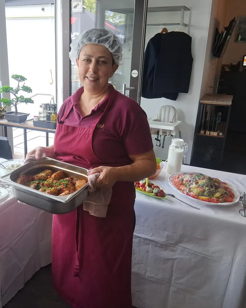 Eine Köchin mit einer Platte Essen vor einem Buffet mit Warmhaltebehältern