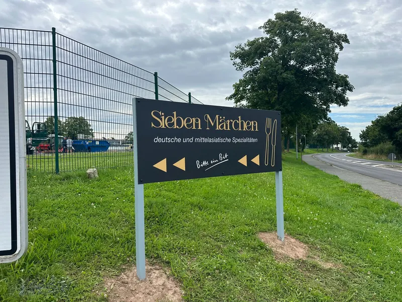 Hinweisschild Sieben Märchen, deutsche und mittelasiatische Spezialitäten, an der Straße